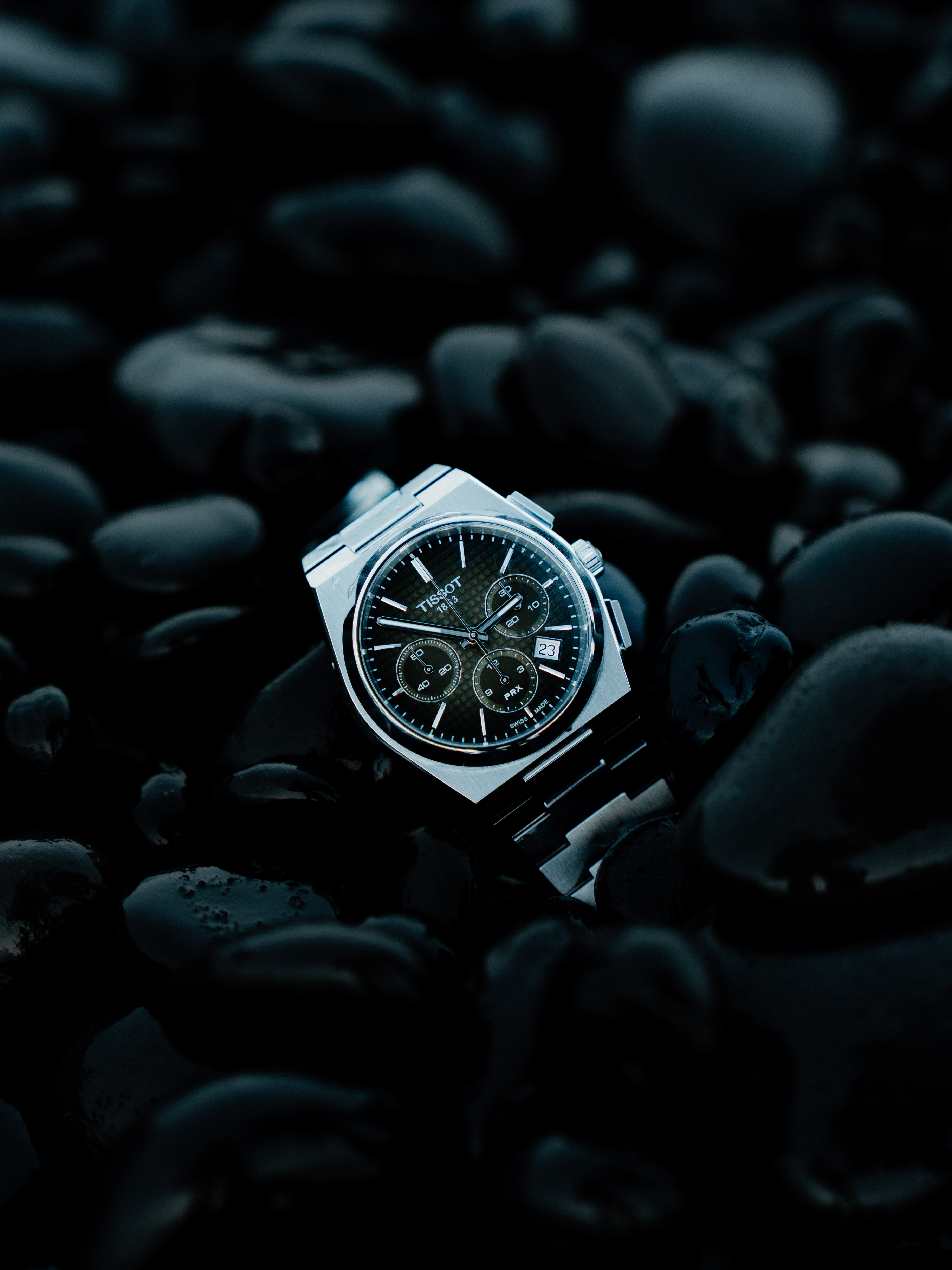 A Tissot watch sits among some shiny black stones